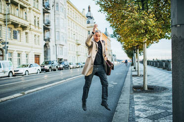 Reifer Geschäftsmann mit Tasche beim Überqueren der Straße in der Stadt Prag, springend. - HPIF28468