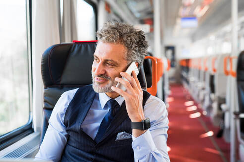 Gut aussehender reifer Geschäftsmann, der mit dem Zug reist. Ein Mann mit Smartphone, der einen Anruf tätigt. - HPIF28475