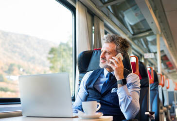 Handsome mature businessman travelling by train. A man with smartphone, making a phone call. - HPIF28476