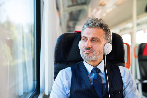 Gutaussehender, reifer Geschäftsmann, der mit dem Zug reist. Ein Mann mit Kopfhörern, der Musik hört. - HPIF28477
