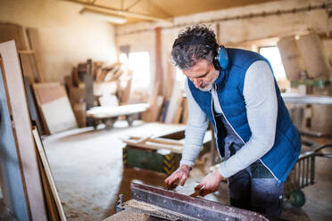 A mature man worker in the carpentry workshop, working with wood. - HPIF28524