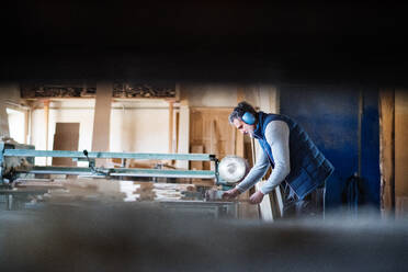 A mature man worker in the carpentry workshop, working with wood. - HPIF28525