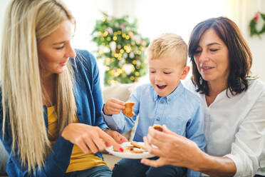 A small boy with mother and grandmother sitting on the sofa at home at Christmas time, eating biscuits. - HPIF28558