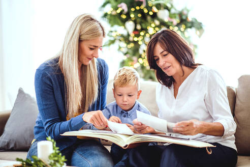 Ein kleiner Junge mit Mutter und Großmutter, die zur Weihnachtszeit zu Hause auf dem Sofa sitzen und sich Fotos ansehen. - HPIF28559