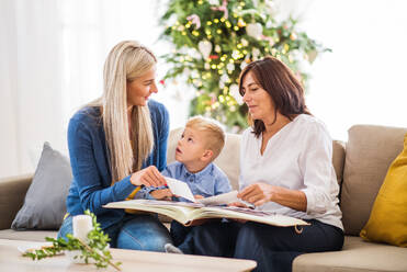 Ein kleiner Junge mit Mutter und Großmutter, die zur Weihnachtszeit zu Hause auf dem Sofa sitzen und sich Fotos ansehen. - HPIF28560