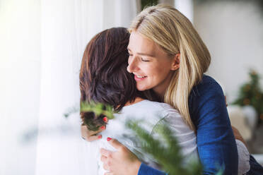 Eine ältere Frau mit ihrer erwachsenen Tochter, die sich zu Weihnachten zu Hause umarmen. - HPIF28576