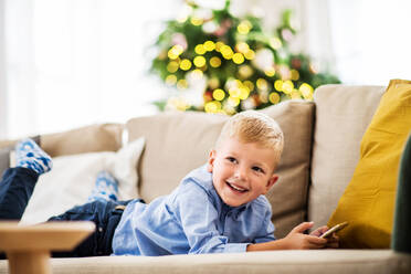 A small boy with smartphone lying on a sofa at home at Christmas time, playing games. - HPIF28579