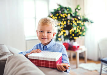 A small boy with a present standing at home at Christmas time. - HPIF28582