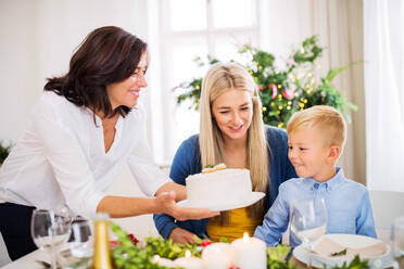 Ein kleiner Junge mit seiner Mutter, der die Großmutter betrachtet, die zu Hause zur Weihnachtszeit einen Kuchen auf den Tisch stellt. - HPIF28584