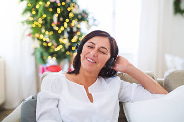 Eine ältere Frau mit Kopfhörern sitzt zu Hause auf dem Sofa und hört Musik zur Weihnachtszeit. - HPIF28588