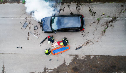 Three unrecognizable firefighters helping a young injured woman lying on the road after an accident. Top view. - HPIF28595