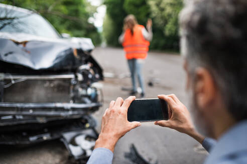 Unbekannter Mann fotografiert ein kaputtes Auto nach einem Unfall. Kopierraum. Eine Fahrerin im Hintergrund. - HPIF28607