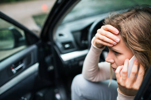 Junge, frustrierte Frau, die nach einem Autounfall im beschädigten Auto sitzt und telefoniert, Nahaufnahme. - HPIF28610