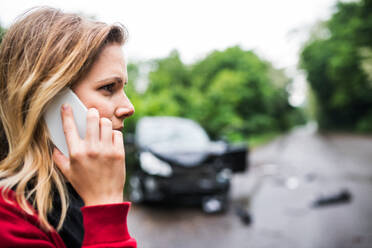 Nahaufnahme einer jungen Frau am Telefon, die nach einem Autounfall neben dem beschädigten Wagen steht; Kopierraum. - HPIF28614