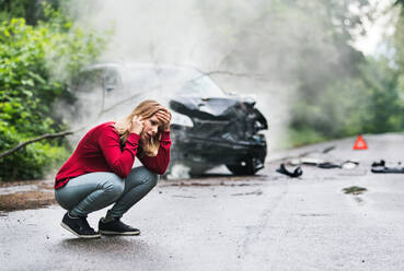 A frustrated young woman with smartphone by the damaged car after a car accident, making a phone call. Copy space. - HPIF28618