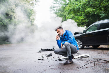 Handsome mature man making a phone call after a car accident, smoke in the background. Copy space. - HPIF28621