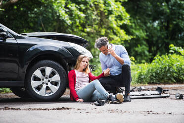 Junge Frau am Auto nach einem Unfall und ein Mann mit Smartphone, der einen Anruf tätigt. - HPIF28631