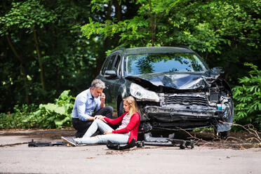 Young woman by the car after an accident and a man with smartphone, making a phone call. - HPIF28632