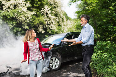 An angry mature man and young woman arguing after a car crash. A smoke coming from a broken car in the background. - HPIF28634