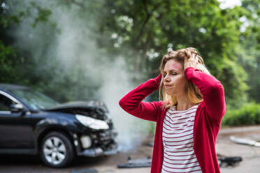 An injured young frustrated woman standing by the damaged car after a car accident. - HPIF28636