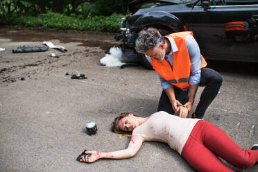 A man helping a young woman lying unconscious on the road after a car accident. Copy space. - HPIF28644