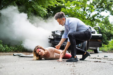 A man helping a young injured woman lying on the road after a car accident. Copy space. - HPIF28645