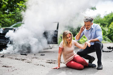 Young woman by the car after an accident and a man with smartphone, making a phone call. - HPIF28647