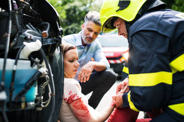 A firefighter helping a young injured woman sitting by the car on a road after an accident, unconscious. - HPIF28650