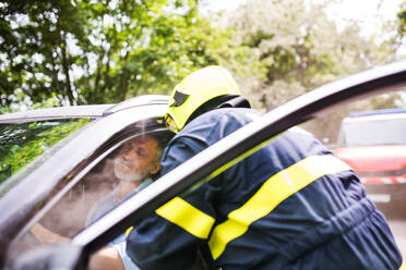 Ein unkenntlicher Feuerwehrmann, der einen bewusstlosen Mann nach einem Unfall aus dem Auto holt. - HPIF28651