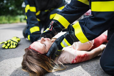 Unbekannte Feuerwehrleute helfen einer jungen verletzten Frau, die nach einem Unfall bewusstlos auf der Straße liegt. - HPIF28655