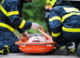 Unbekannte Feuerwehrleute legen eine junge verletzte Frau nach einem Autounfall auf der Straße in eine Plastiktrage, Nahaufnahme. - HPIF28660