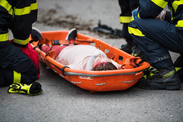 Unbekannte Feuerwehrleute legen eine junge verletzte Frau nach einem Autounfall auf der Straße in eine Plastiktrage, Nahaufnahme. - HPIF28663