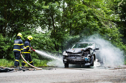 Zwei Feuerwehrleute löschen ein brennendes Auto nach einem Unfall auf der Landstraße. - HPIF28666