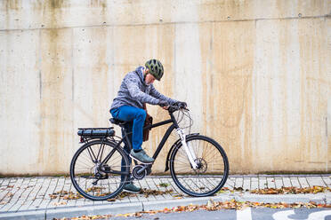 Aktiver älterer Mann mit Elektrofahrrad im Freien stehend in der Stadt. Raum kopieren. - HPIF28674