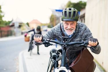 Active senior couple with helmets and electrobikes standing outdoors on a road in town. - HPIF28676