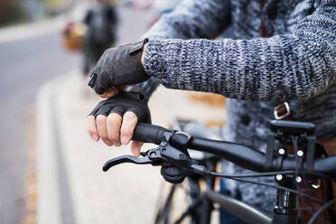 A close-up of a cyclist with electrobike putting on black gloves outdoors in town. - HPIF28677