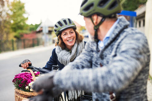 Aktives Seniorenpaar mit Helmen und Elektrofahrrädern, die im Freien auf einer Straße in der Stadt stehen. - HPIF28678