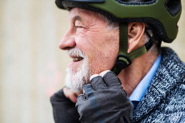 Nahaufnahme eines aktiven älteren Mannes mit Bart und Schnurrbart, der im Freien steht und einen Fahrradhelm aufsetzt. - HPIF28682
