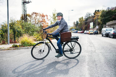 Ein aktiver älterer Mann mit Helm und Elektrofahrrad fährt im Herbst in der Stadt im Freien. - HPIF28699