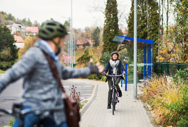 An active senior couple with helmets and electrobikes cycling outdoors on a pathway in town. - HPIF28700