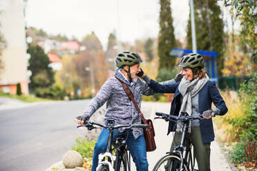 Happy active senior people with electrobikes greeting outdoors on a road in town. - HPIF28702