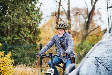 An active senior man with helmet and electrobike cycling outdoors in autumn in park. - HPIF28705