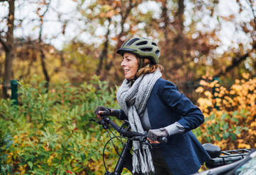 An active senior woman with helmet and electrobike cycling outdoors in autumn in park. - HPIF28706
