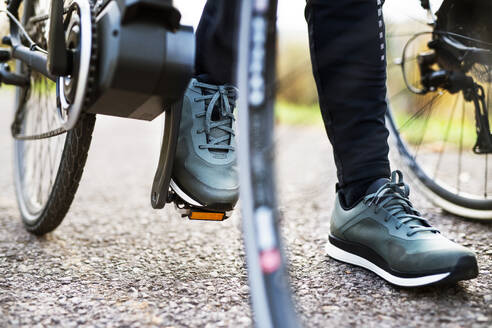Eine Nahaufnahme von Beinen und Füßen auf dem Pedal eines Elektrofahrrads im Freien auf einer Straße im Park. - HPIF28734