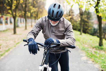 Ein aktiver älterer Mann mit Helm und Elektrofahrrad steht im Freien auf einer Straße in der Natur. - HPIF28735