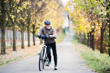 Ein aktiver älterer Mann mit Helm und Elektrofahrrad steht im Freien auf einer Straße in der Natur. - HPIF28736