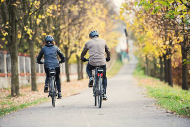 Rückansicht eines aktiven Seniorenpaares mit Elektrofahrrädern, das im Freien auf einer Straße radelt. - HPIF28740