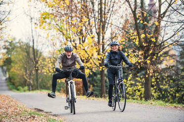 Ein aktives Seniorenpaar, das mit Helm und Elektrofahrrädern draußen auf einer Straße in der Natur radelt und Spaß hat. - HPIF28741