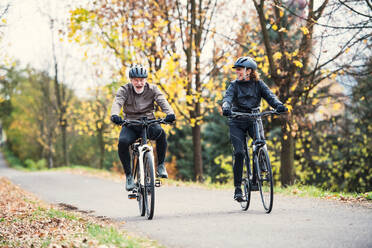 Ein aktives Seniorenpaar mit Elektrofahrrädern fährt im Herbst auf einer Straße im Park. - HPIF28742