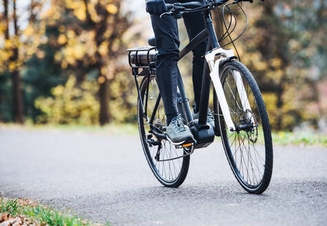 Ein unkenntlicher Mann auf einem Elektrofahrrad fährt im Freien auf einer Straße in einem Park. - HPIF28743